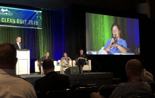 Woman speaking on a panel with her image projected onto a screen.