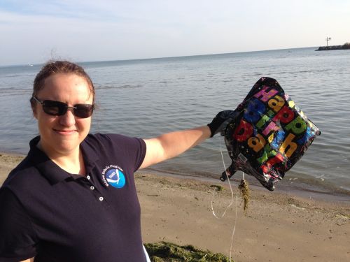 A woman on a beach holding a deflated "Happy Birthday" balloon.