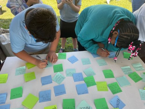 Two kids writing on sticky notes.