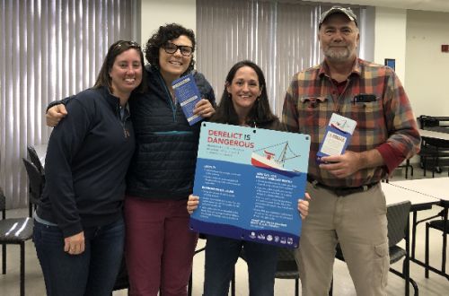 Group of four people pose with a sign.