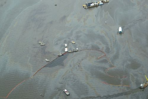 Overhead view of water with response vessels, boom and oily sheen.