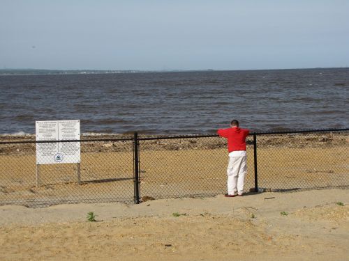 Beach with a fence, sign, and person looking out at water.