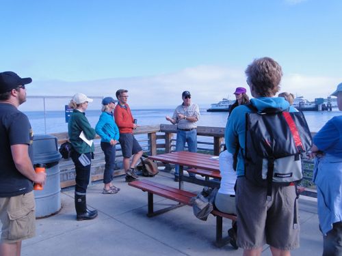 People standing on a dock, listening to someone speak.