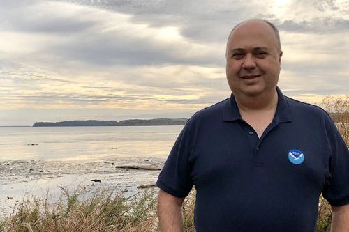 A person posing for a photo in front of a body of water.