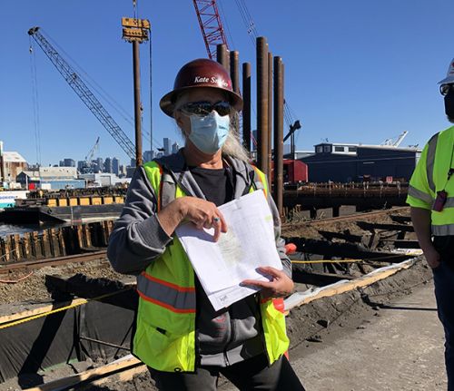 Woman in safety vest gesturing to a paper in her hand.