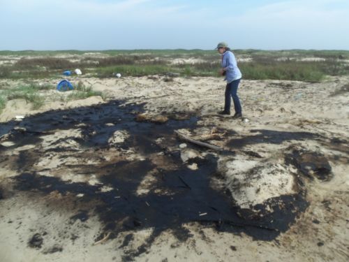 Person on a beach littered with oily material.