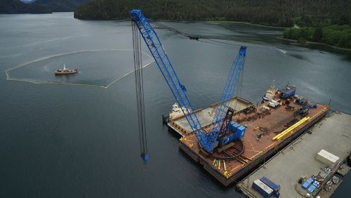 Aerial photo of vessel surrounded by boom with heavy equipment on a dock.