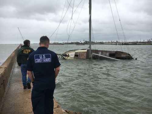 Two men on a dock; sailboat capsized in water. 