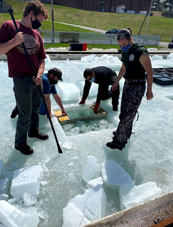 People standing on ice with a square cut into the ice.