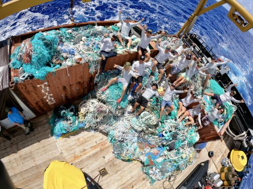 A group of people on a pile of garbage bags and debris on a boat.