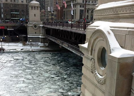 Ice on a river with a bridge crossing it in a city.