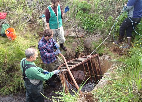 Workers removing trash rack from stream.