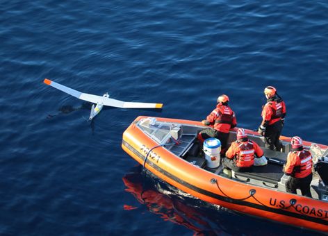 People in a boat next to a small unmanned plane in the water.