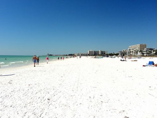 People walking on a developed portion of white sand beach at the ocean.