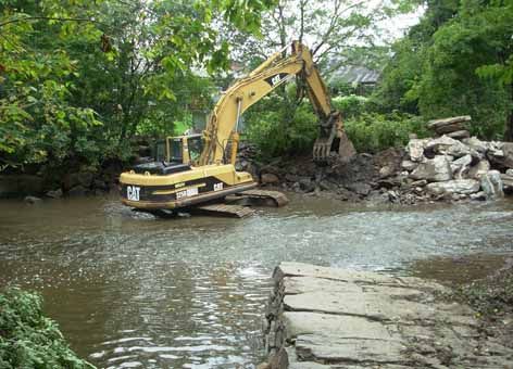 Excavator removes a rock dam from a stream.