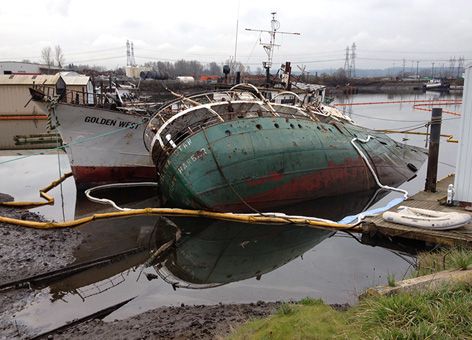 Two rusted ships partially sunk in water and surrounded by containment boom.