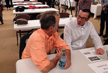 Two men sit at a table talking.