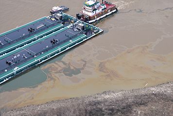 Barge leaking oil in river next to towboat.