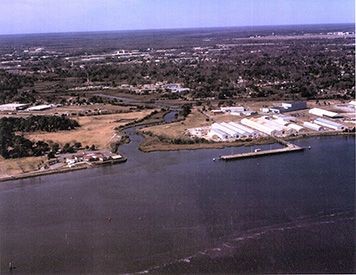 An aerial view of the former Navy base and the Cooper River (foreground) looking up Noisette Creek, dating to approximately 2003. The area restored back to coastal wetlands appears on the left side of the creek. The project site starts where the parking lot ends and extends to the first road crossing the creek. (The Noisette Company/Jim Augustin) An aerial view of the former Navy base and the Cooper River up Noisette Creek.