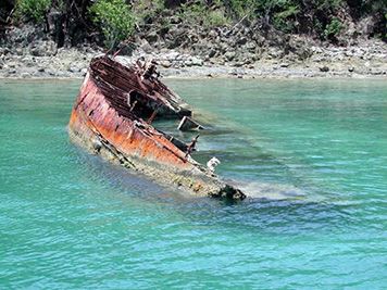 A partially submerged, rusted-out sailboat.