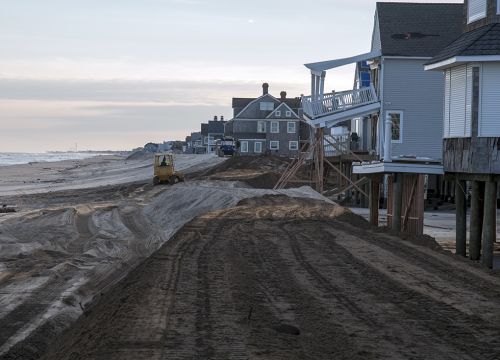 Machines moves sand to rebuild a New Jersey beach by Sandy-damaged houses.