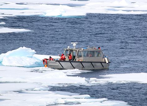 People in a boat lowering orange ball into icy waters.