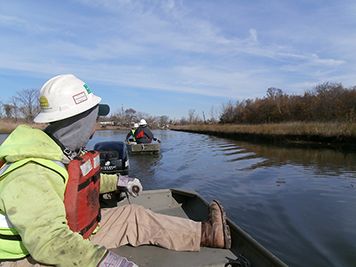 Men driving small boats up a marshy creek in winter.