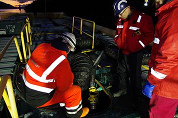 Several men work to pump oil onto a barge on the ocean.