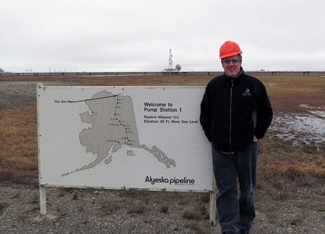 Man in hard hat outside at sign at start of Trans Alaska Pipeline.