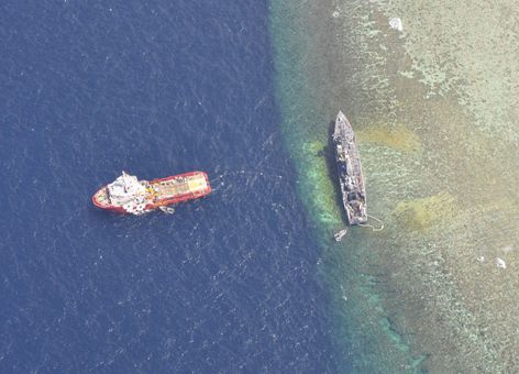 USS Guardian grounded on coral reef with tug removing fuel and wastewater.