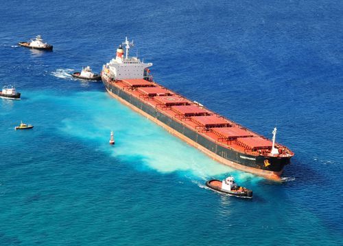 Surrounded by response vessels, the cargo ship Vogetrader grounded on coral.