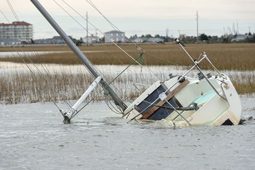 An abandoned and derelict vessel submerged in a marsh with buildings in the distance.