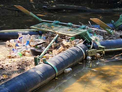 A trash trap device installed in a river that has captured plastic bottles and other marine debris to prevent it from traveling to other areas.