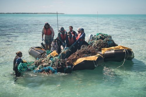 A team of people hauls a mass of derelict fishing nets off reefs from a small inflatable vessel.
