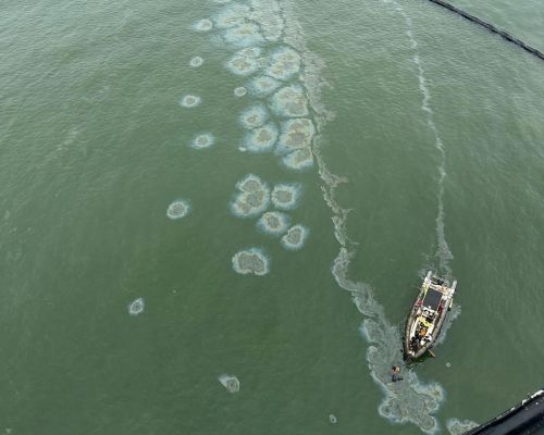 Aerial image of oil emerging in an area of containment boom. A response vessel is seen in the lower right of the image.