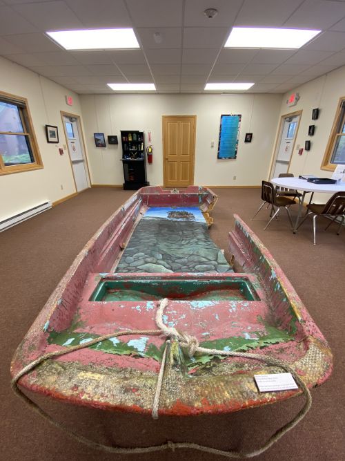 A broken boat staged in the center of a room within an aquarium.