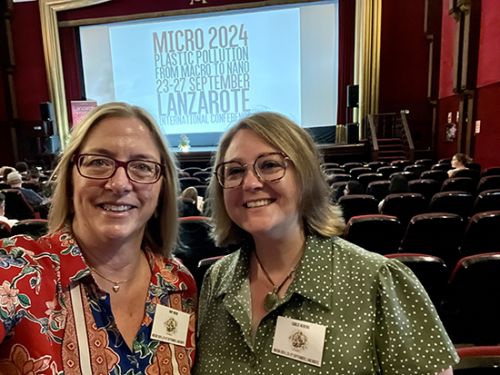 Two individuals take a selfie in front of a presentation screen.