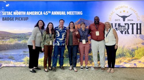Individuals stand in a group and smile in front of an Society of Environmental Toxicology and Chemistry-themed backdrop.