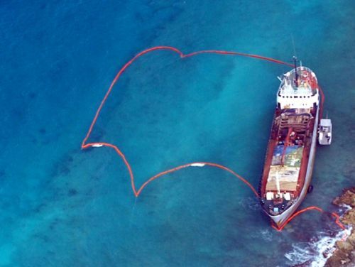 A ship run aground on coral reef, surrounded by protective oil boom.