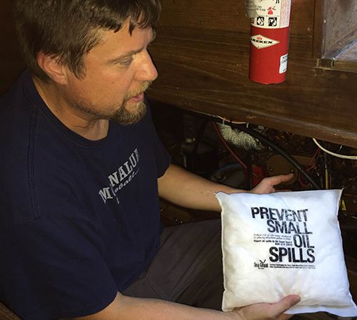 Man holding pillow-shaped absorbent pad near boat bilge.