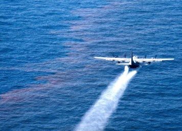 Aircraft flies over oil floating on the surface of the ocean.