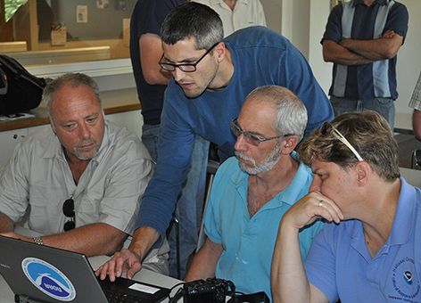 Four individuals direct their attention to a laptop computer screen.