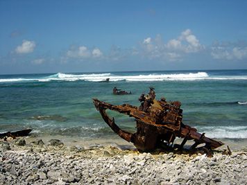 Rusted debris from a grounded vessel sets on the beach and in the surf.