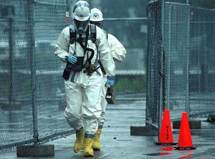 Two emergency responders in protective clothing walk past a fenced area.