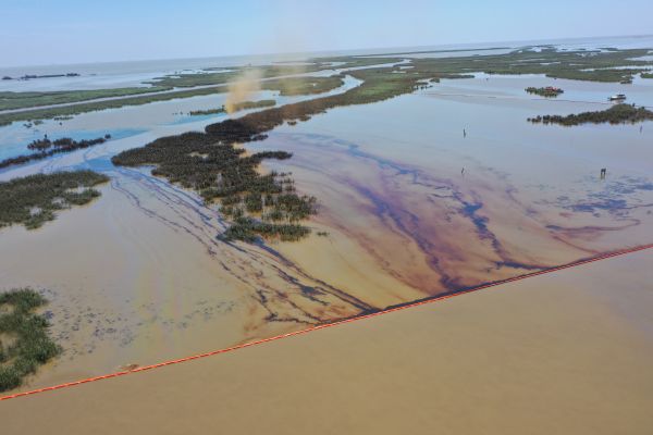 An overflight image displays an oil spill in a coastal marsh environment with floating boom present to contain released oil.