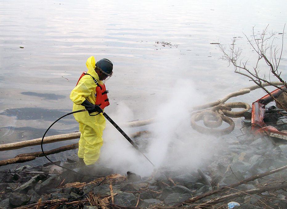 Worker spray-cleaning oily rocks.