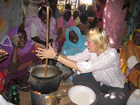 Woman with cooking pot, surrounded by a group of people.