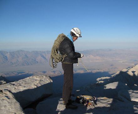 Woman standing on a mountain top with climbing equipment.