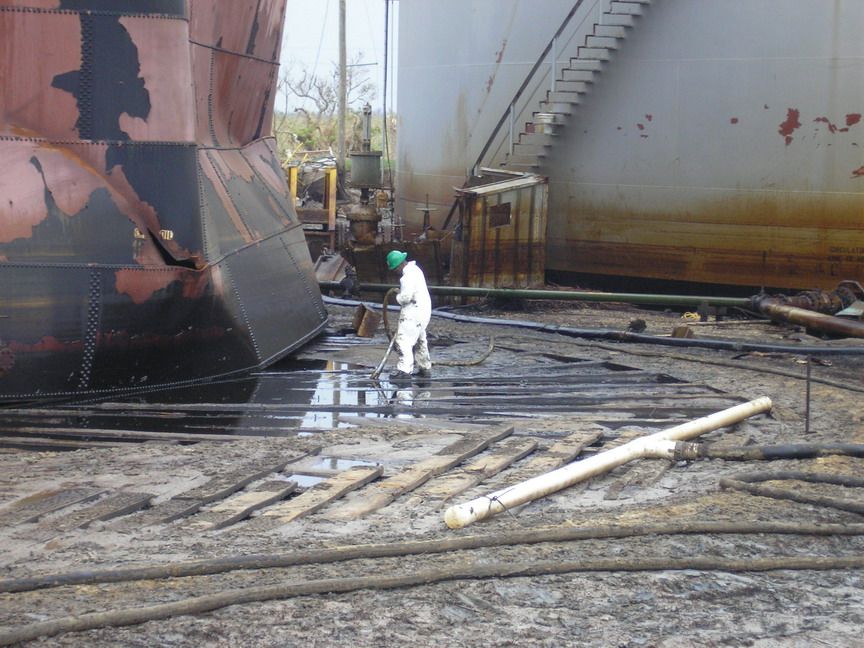 Worker vacuuming oil next to large tank.