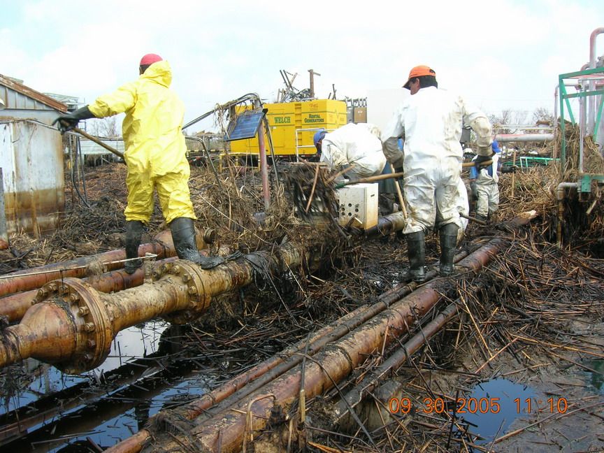 Workers cleaning oil from pipes on the ground.